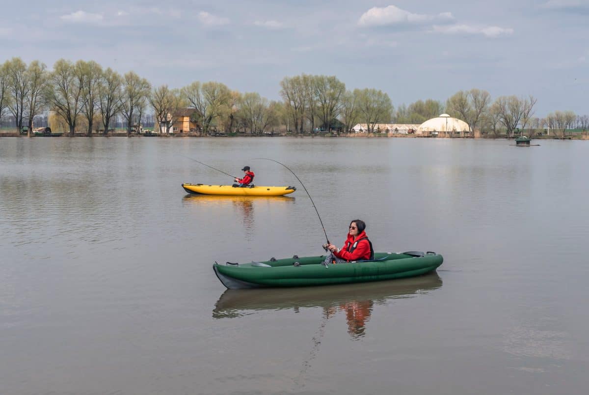 Kayak fishing at lake. Two fisherwomen on inflatable boats with fishing tackle.
