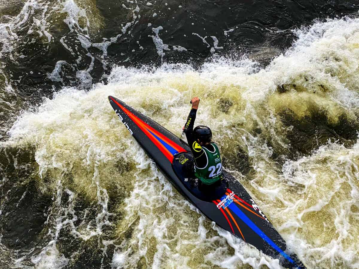 Man paddles black whitewater kayak, with red stripe, through rapids