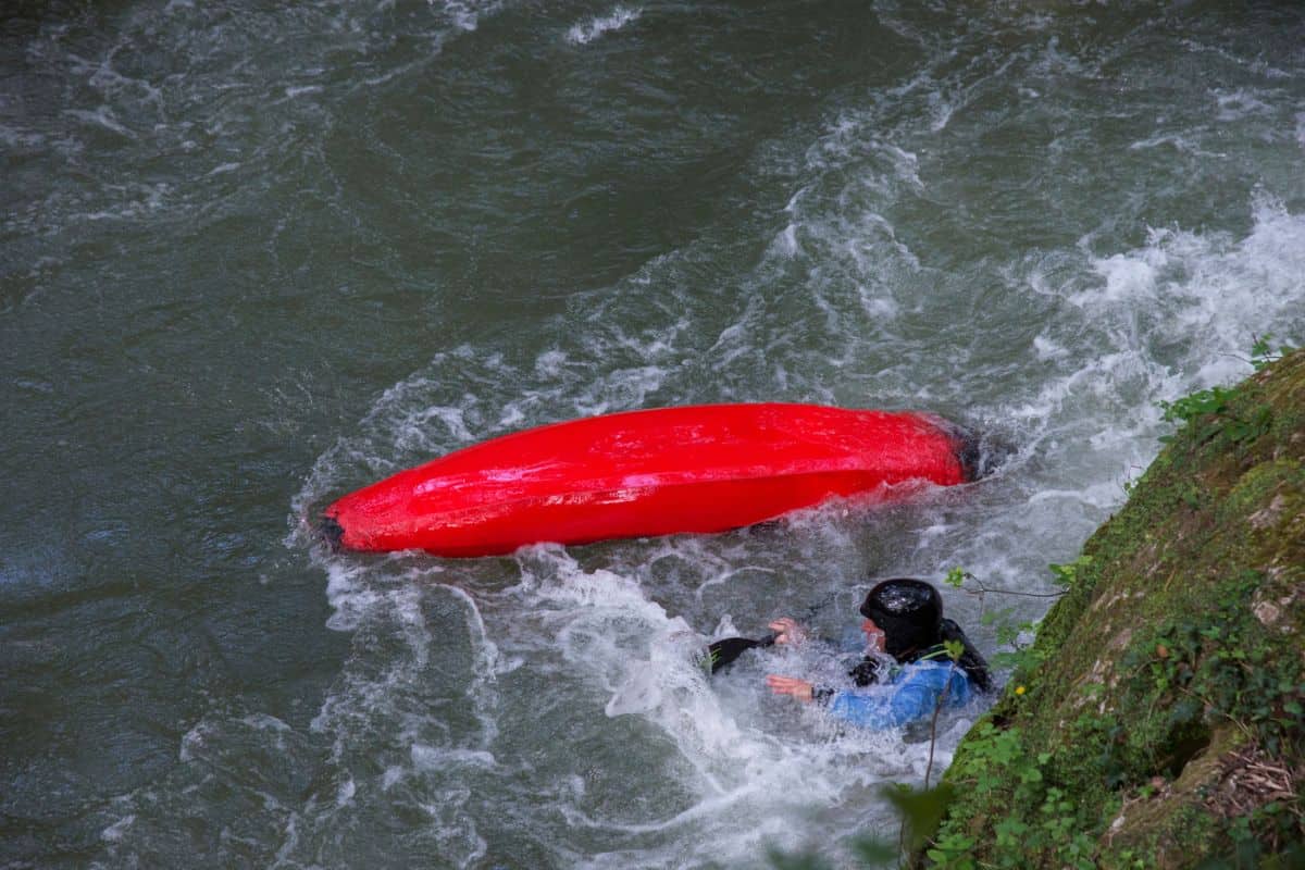 Capsized red kayak with man in water after wet exit