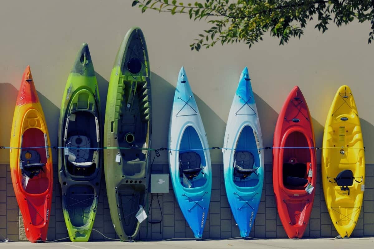 Collection of brightly colored sit in and sit on top kayak stood against a wall