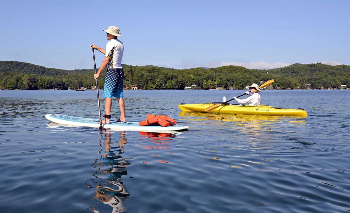 Couple recreational paddling for exercise, man paddleboarding and woman kayaking on a beautiful lake.