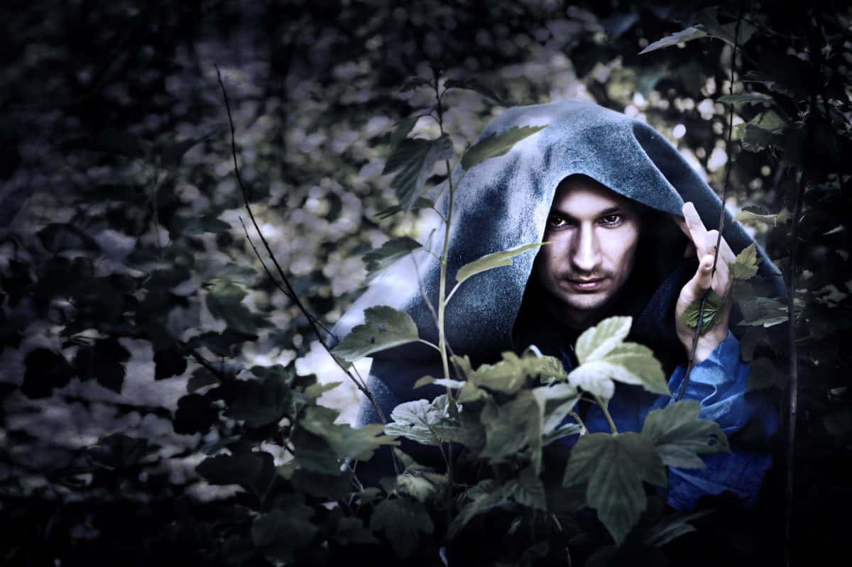 Mystery man in a raincoat with a hood hiding in the trees