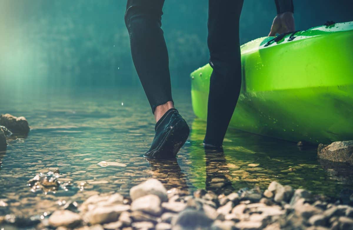 Man wearing kayaking shoes pushing green kayak into water