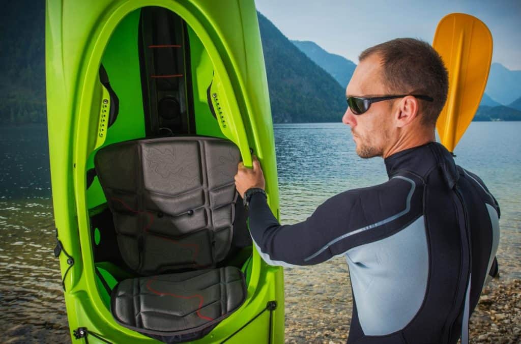 Man holding green kayak wearing black wetsuit