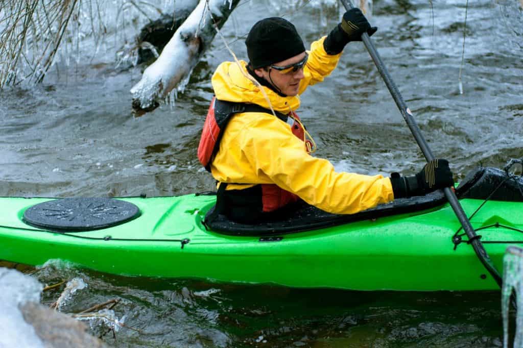 Man in yellow kayak dry suit paddling green kayak in cold water