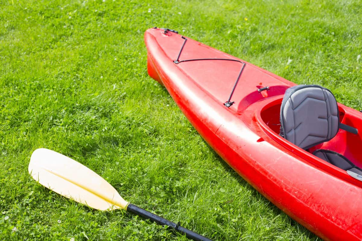 Red lightweight kayak and yellow row lays on the green grass 