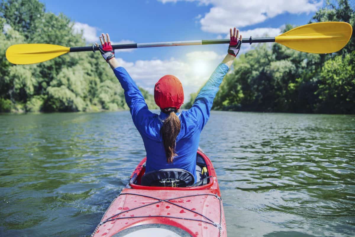 A girl paddles a red kayak on a river in a sunny day