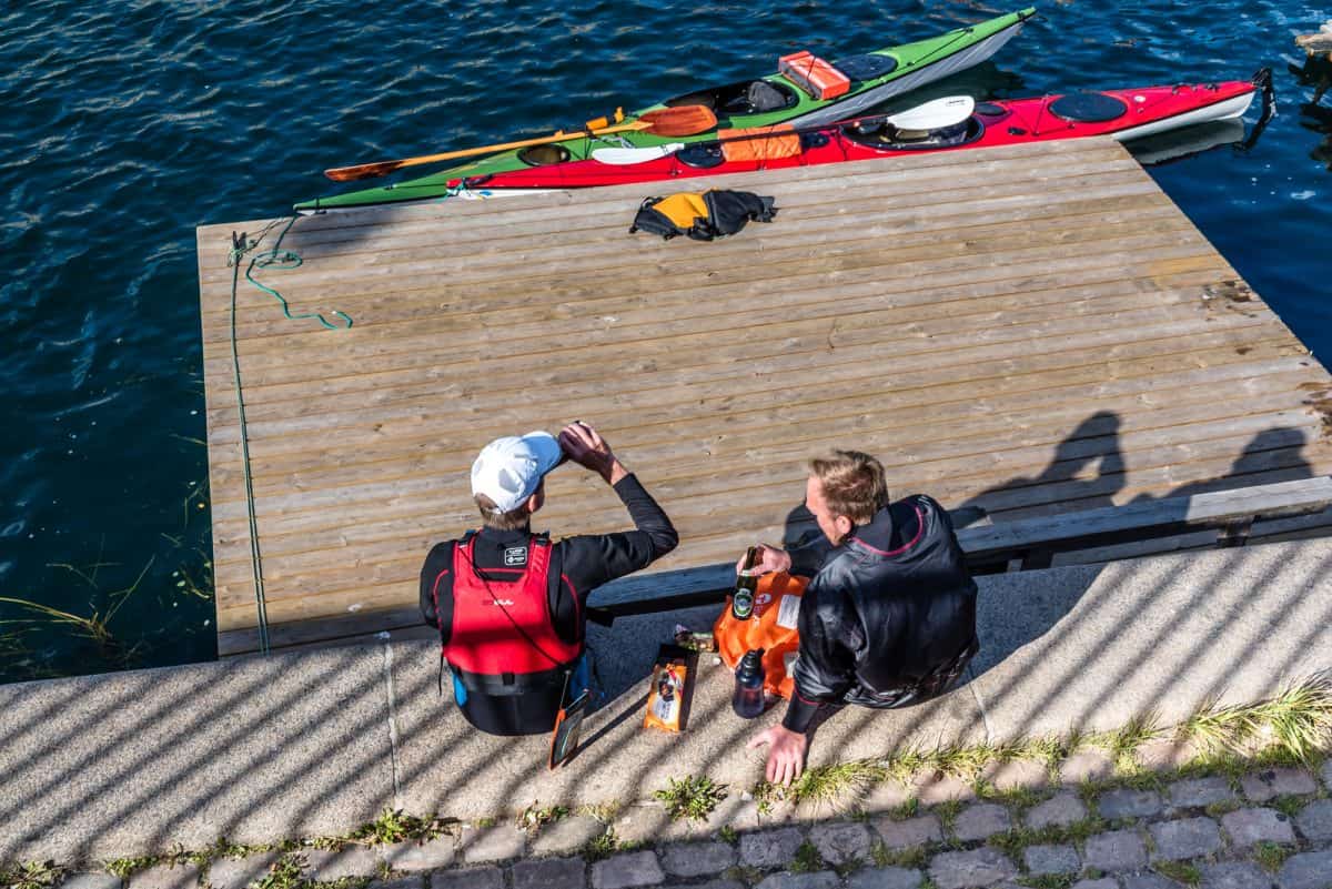 Canoeists resting after exercise and drinking beer sitting on water edge