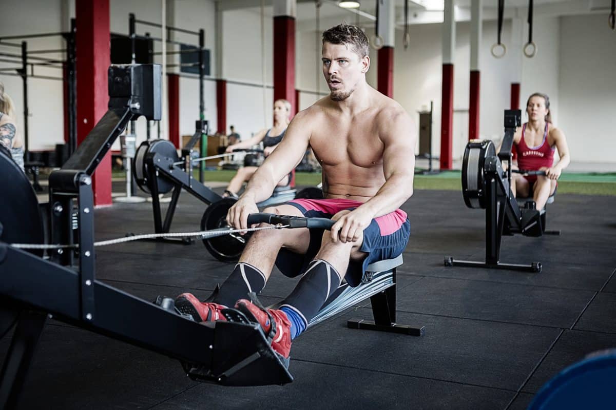 Full length of young shirtless man using rowing machine in gymnasium