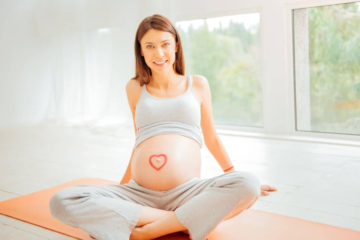 Kayaking While Pregnant Love my baby. Satisfied impregnate pleasant woman sitting on the gymnastic rug looking straight and smiling.