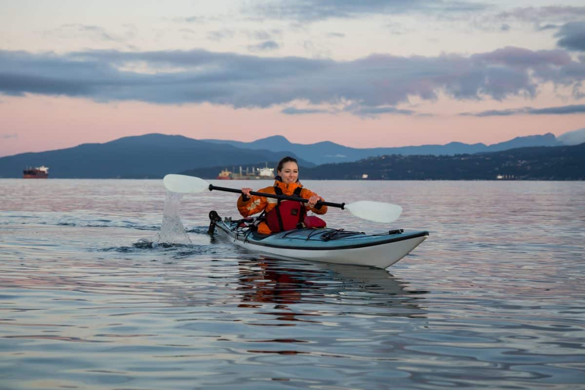 Womwn in rwd drysuit paddling white and blue kayak