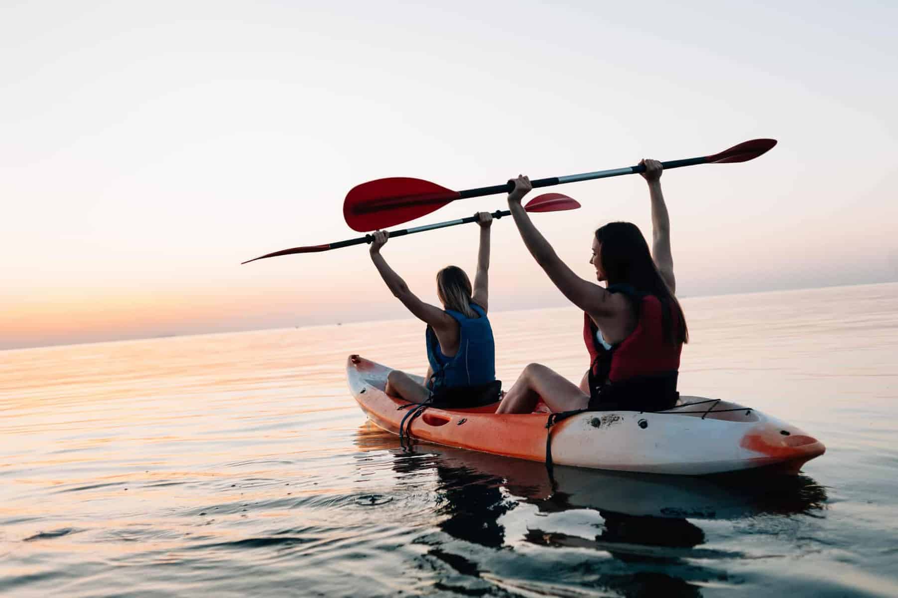 Two females holding kayak paddle above head