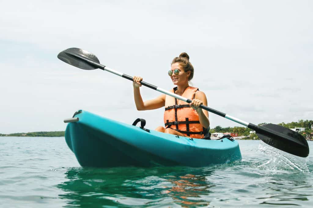 Girl paddles in orange kayak life vest 