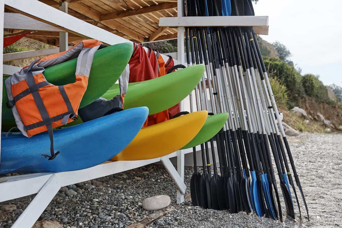 Kayaks, life jackets, oars under a wooden storage rack on the beach