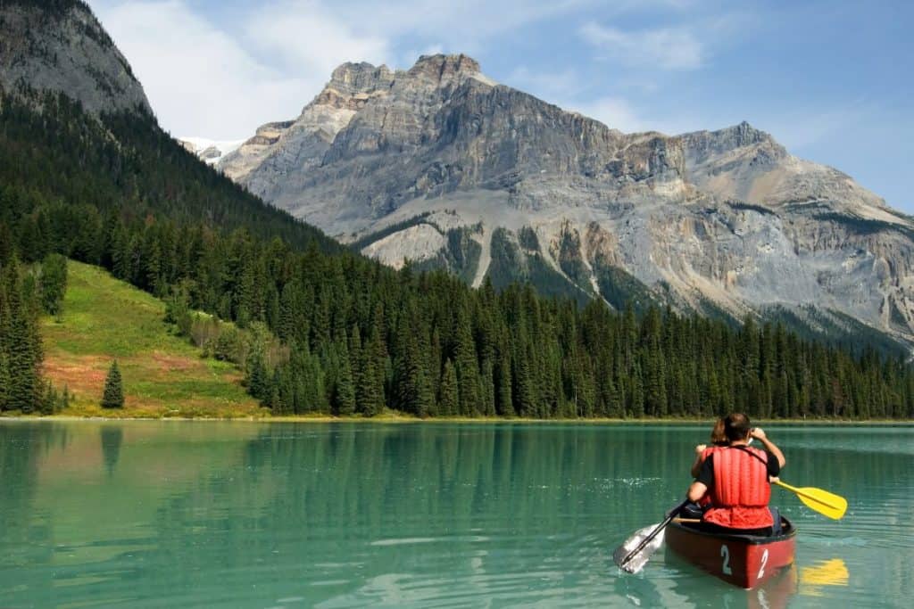 man in orange life vest kayaks on pretty lake with mountain background