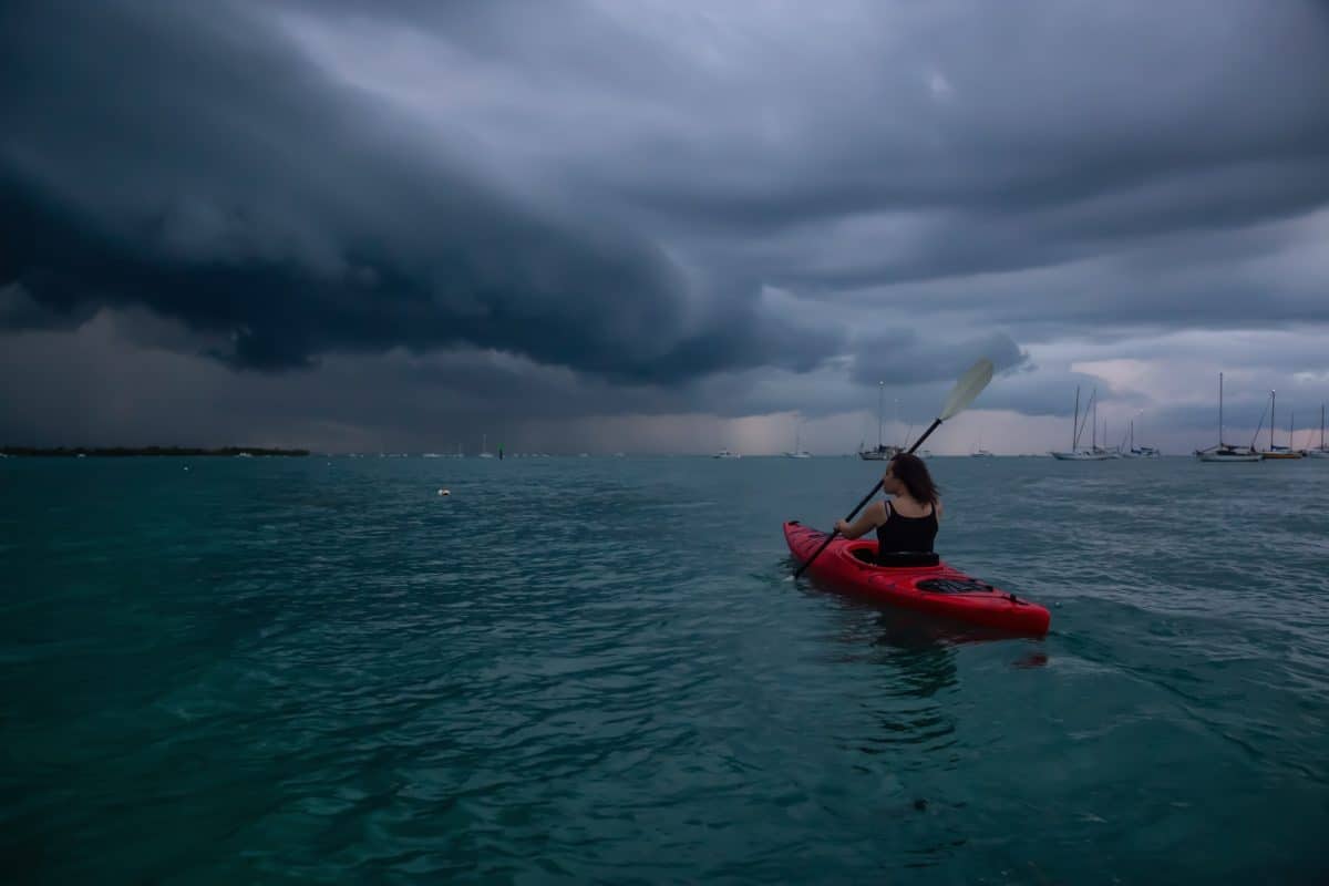 Adventurous girl on a red kayak is kayaking towards a thunderstorm