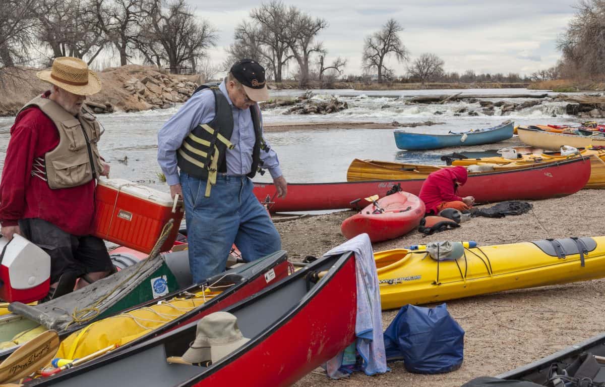 two gents carry seattle sports kayak cooler surrounded by multicolored kayaks.