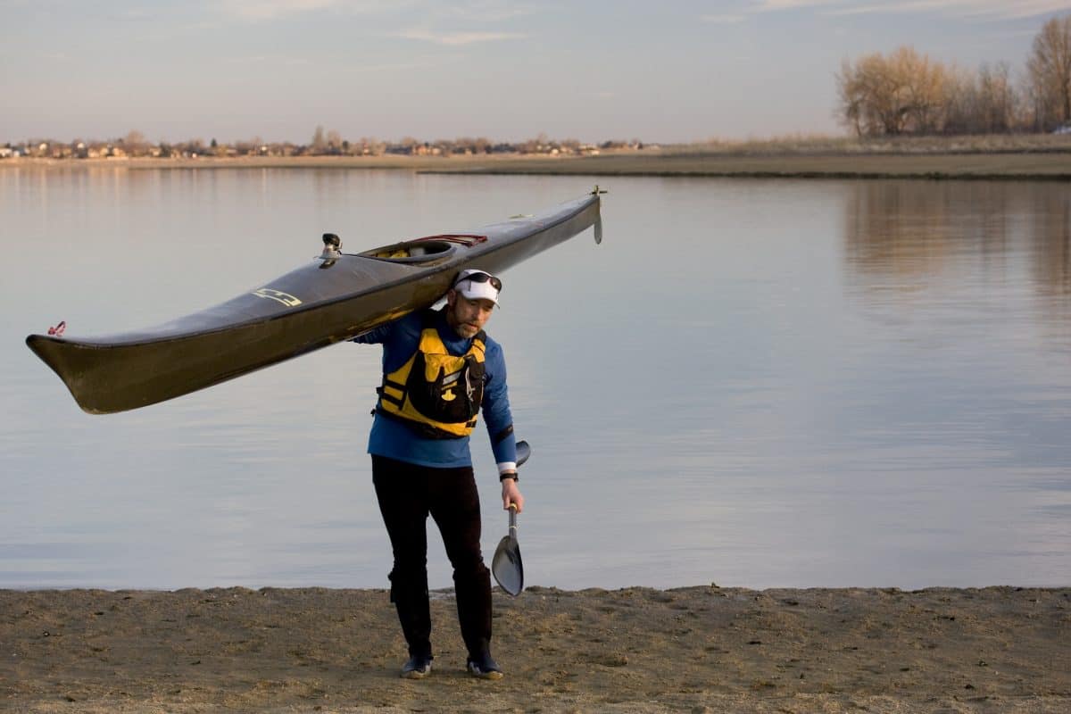 man carries from the water a grey kayak on his shoulder