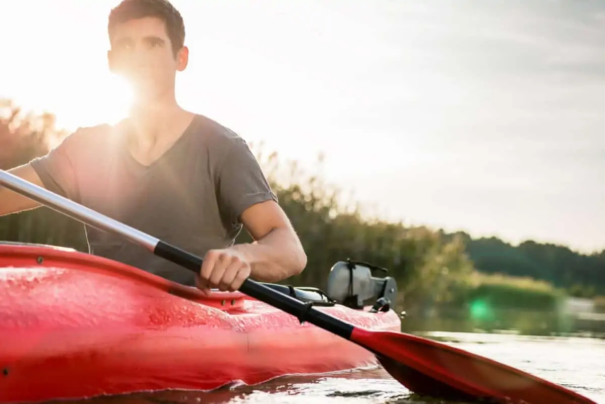 Man with red paddle kayaking in sunny day on lake