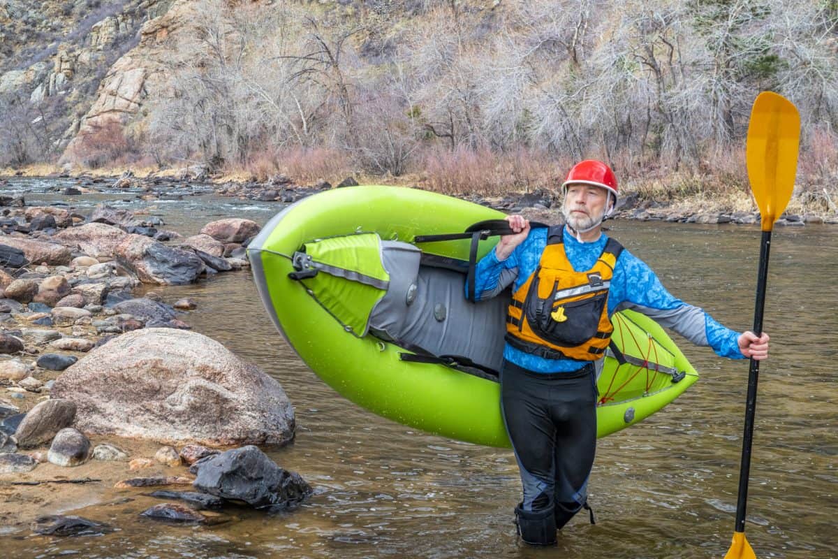 Man wearing a kayaking boots carries kayak on shoulder 