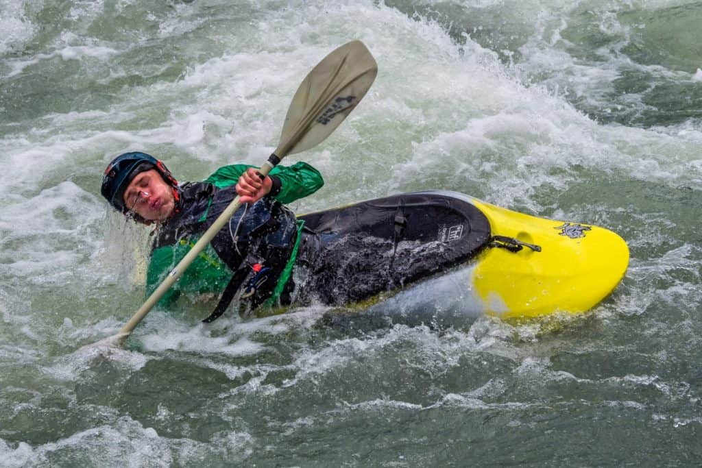 Man in yellow whitewater kayak, wearing green dry suit, rolling in rapids