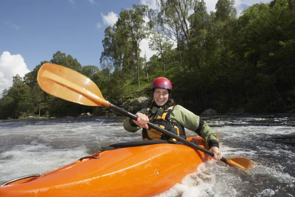 women in green dry suit upstream paddling in orange kayak