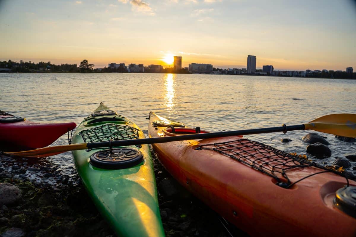 kayak in front of a sunset, kayaks with the skyline of Helsinki in the background, sunset behind Espoo laguuni, golden hour sunset,