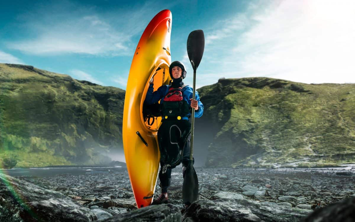 Man poses at water edge hilding yellow kayak, dressed in drysuit