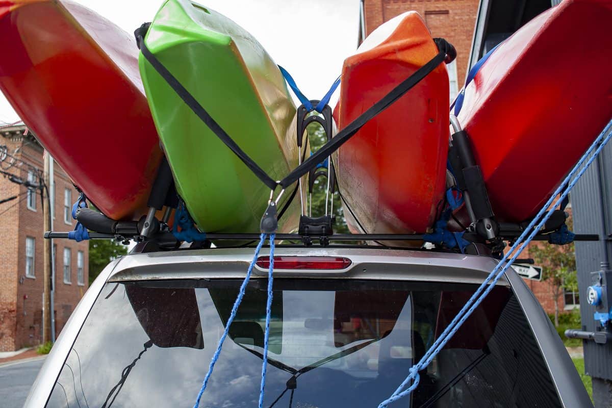 Four red and green colored full size kayaks loaded on top of an SUV car using a combination of tie down straps and roof mounted cross bars.