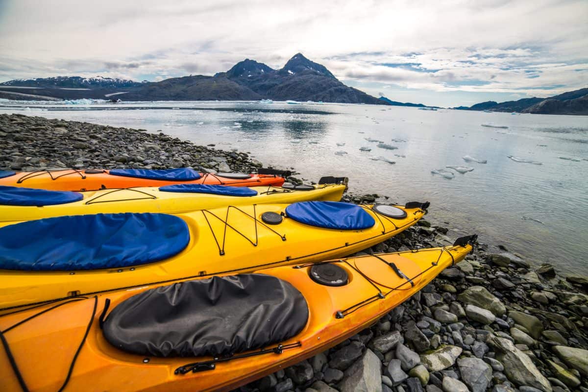 Three Yellow plastic kayaks laying on pebble shoreline with spray skirts and drop down skeg