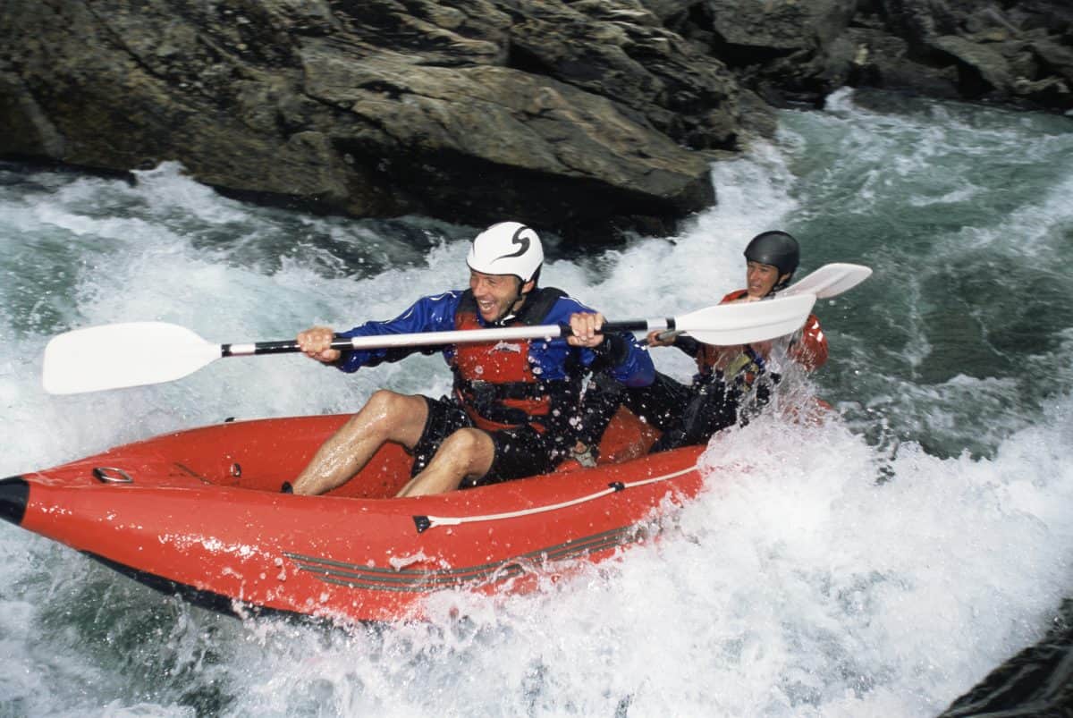 best inflatable kayaks - man paddles in orange inflatable in rapids