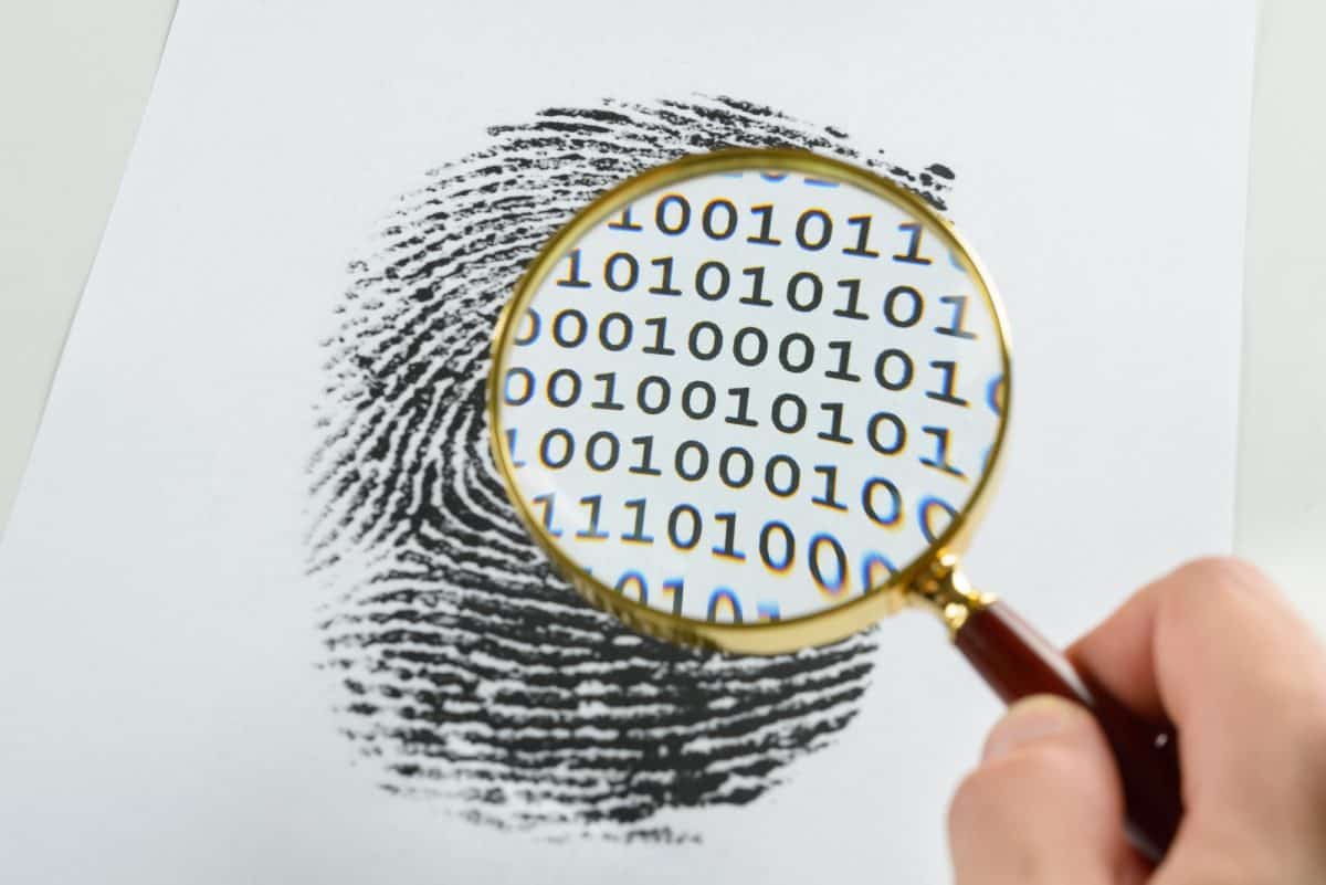 Person Hand With Magnifying Glass Over A Finger Print Revealing Binary Code Within The Print