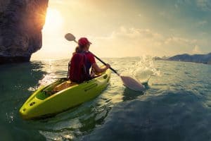 Young lady paddling the kayak near the cliff at sunset