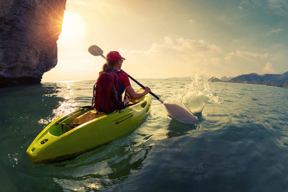 Young lady paddling the kayak near the cliff at sunset