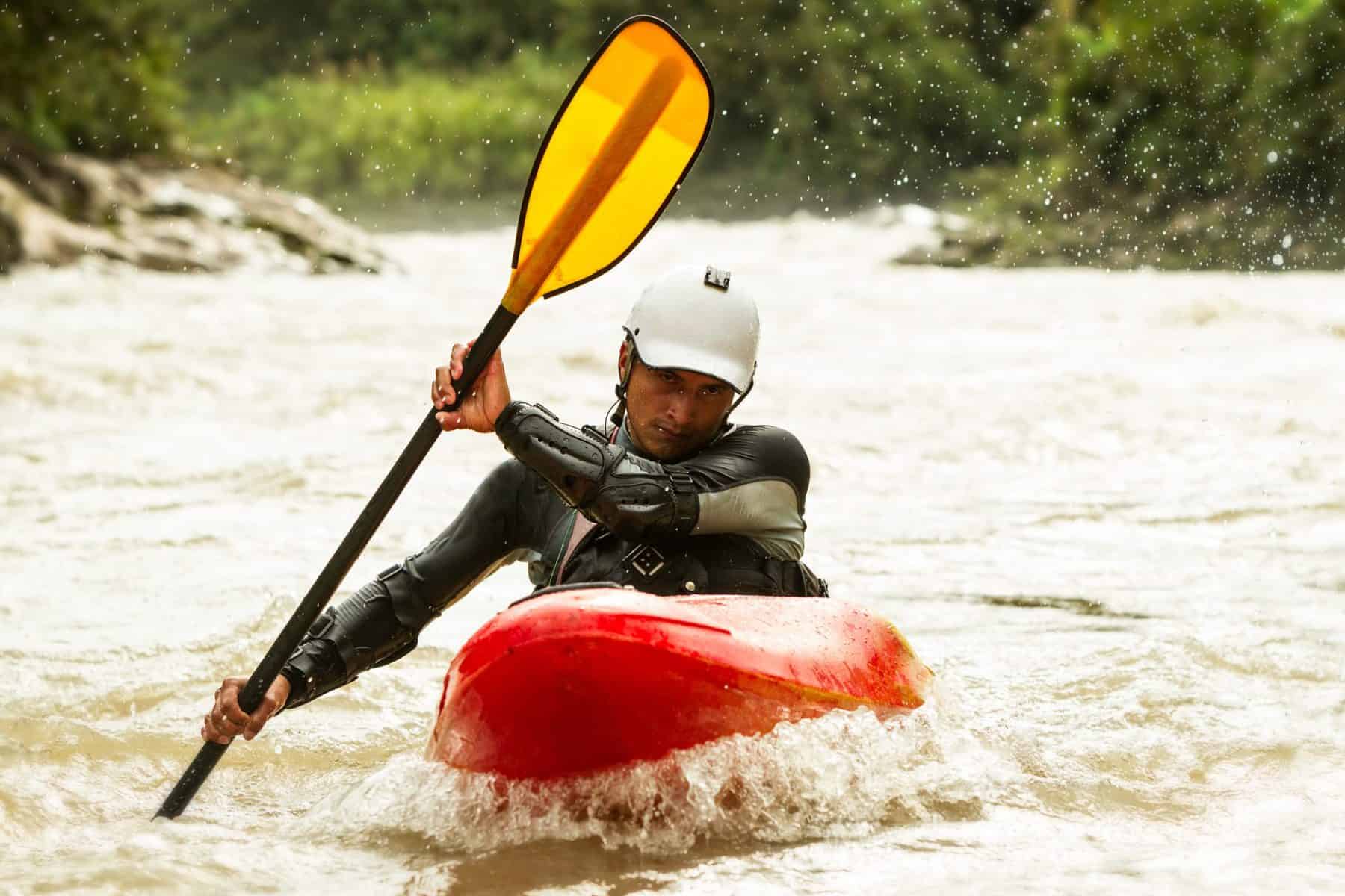 Whitewater kayaker in full gear holding yellow paddle