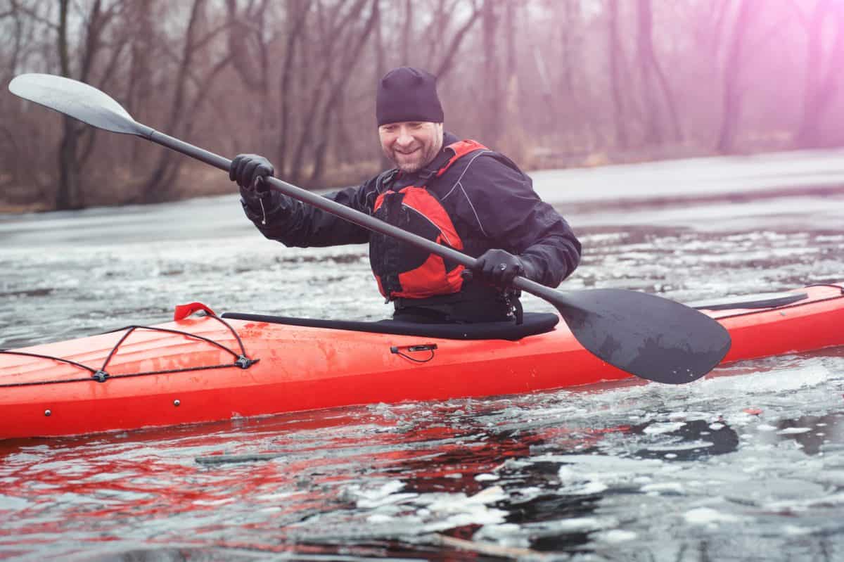 Cheerful Man in drysuit paddling orange kayak