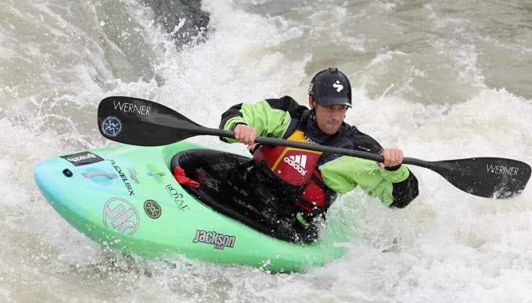 man fights whitewater rapids in green playboat