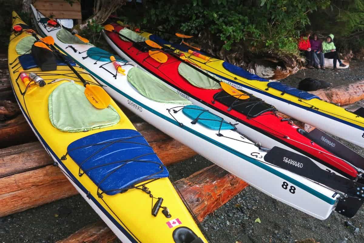 Four brightly colored kayaks on the shore in the rain, with cockpit covers on to prevent the rain getting in