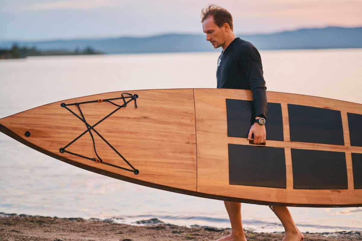 Man Carrying underarm a Wooden sup on sandy beach