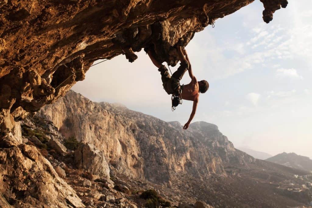 Man hanging off cliff one handed rock climbing
