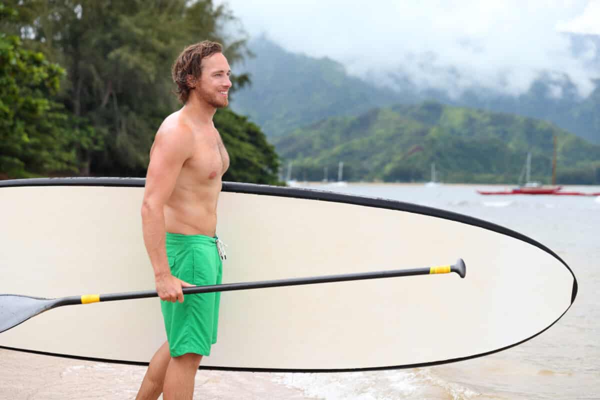 Man holding SUP paddle with paddle board under left elbow