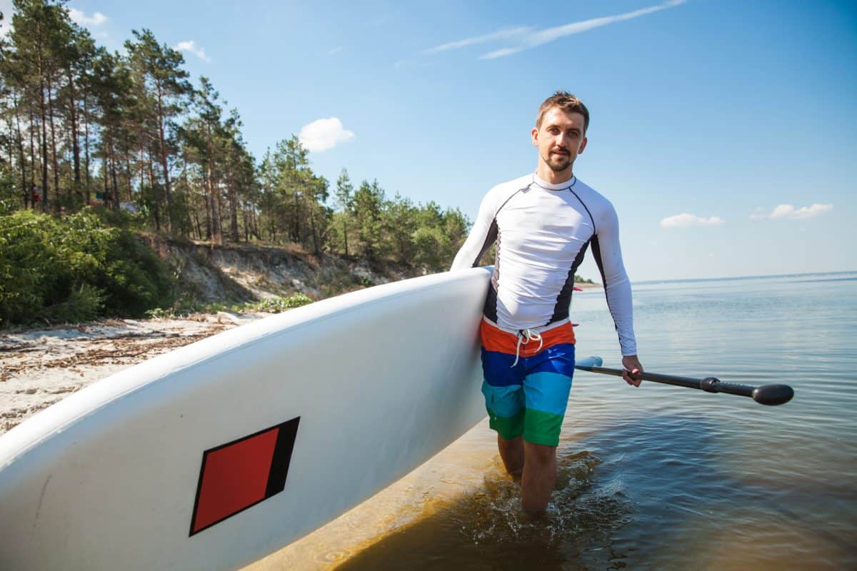 Man in rash vest carrying SUP on beach