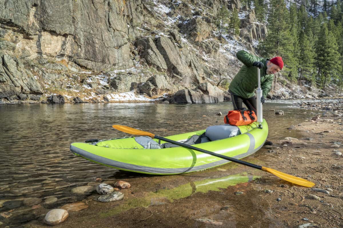 Man in red hat pumping up inflatable whitewater kayak