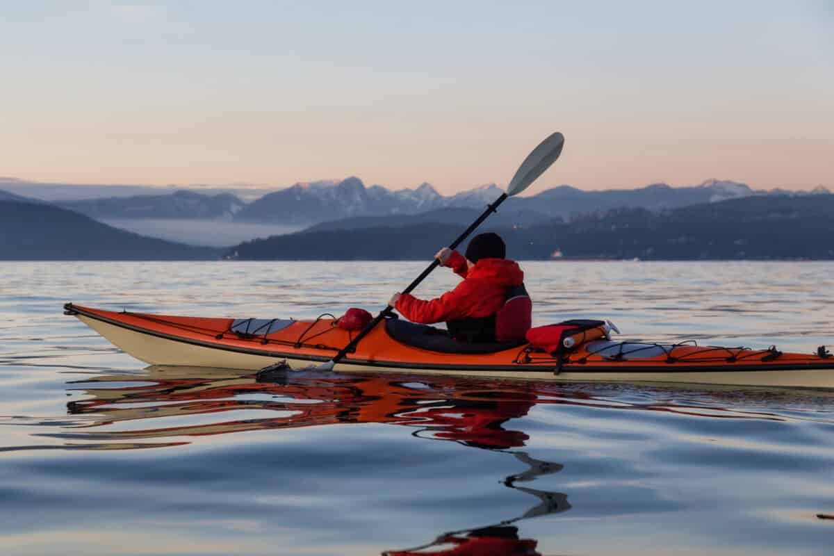 Man in sea kayak paddling on open water during cold weather