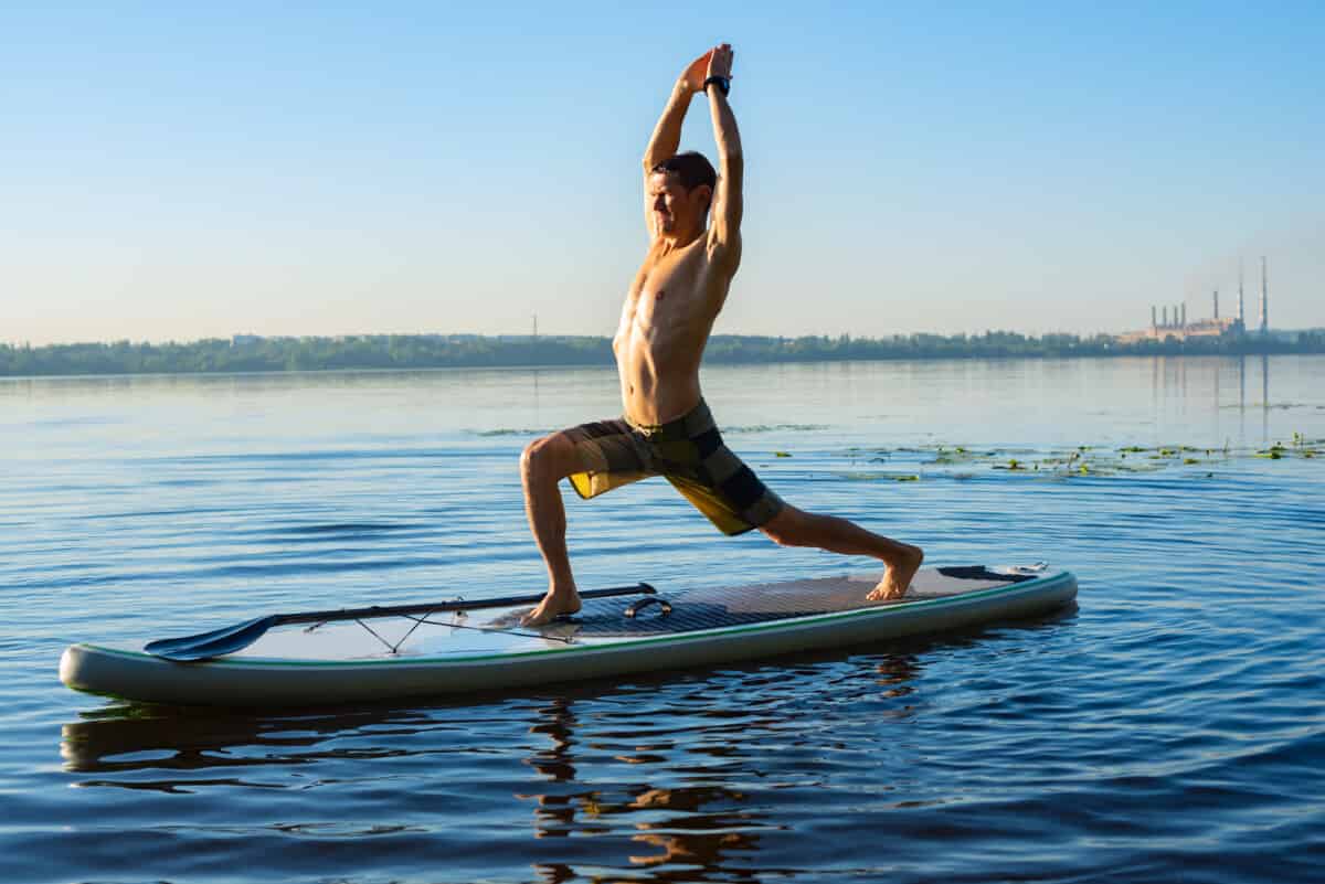 Man on stand up paddle board in deep squat with right and left hand above head