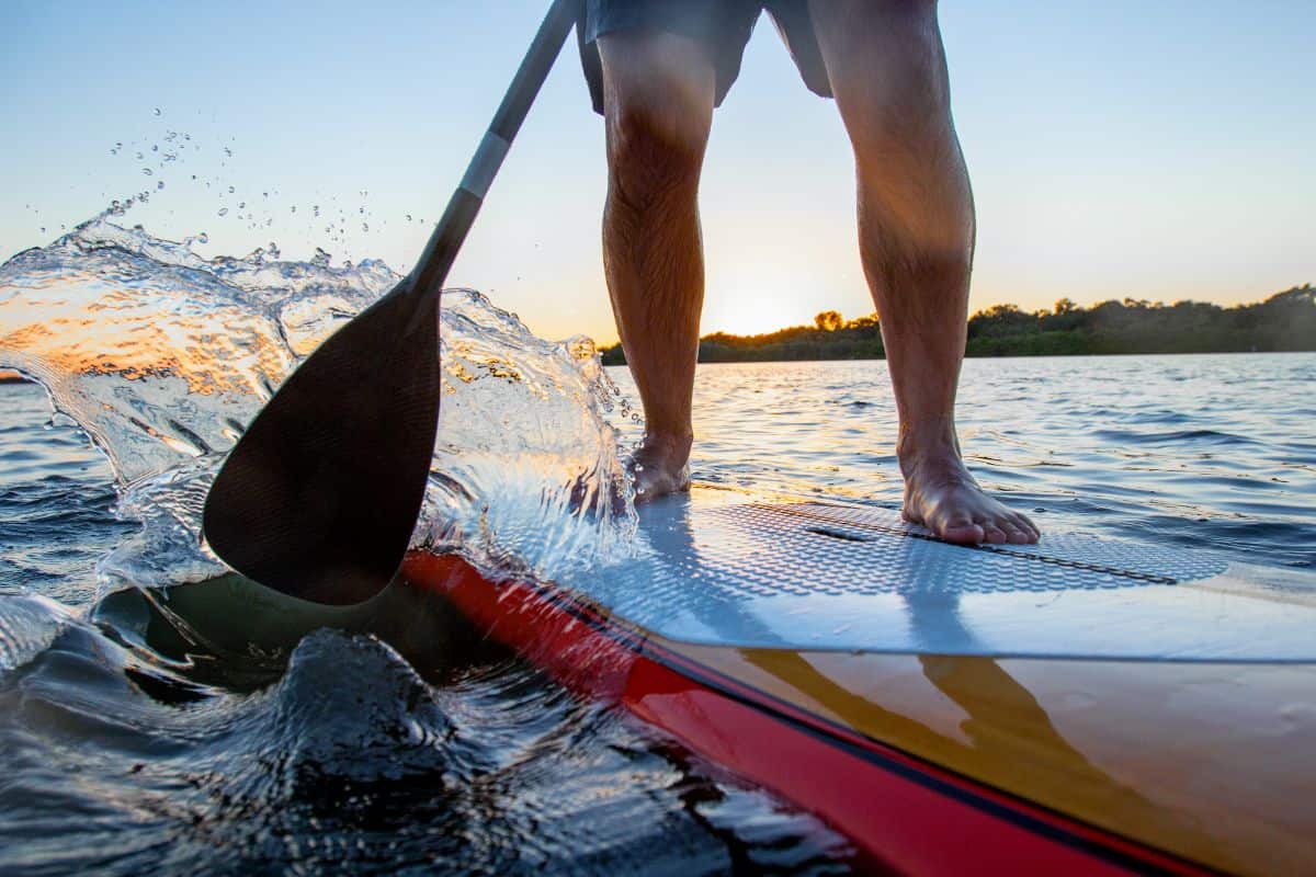 Man on standup paddleboard with carbon SUP paddle blade splashing water due to intense paddling technique