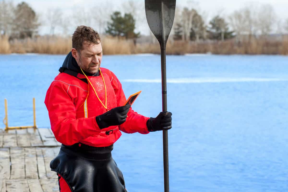 Man wearing red dry suit and neoprene gloves holding kayak paddle