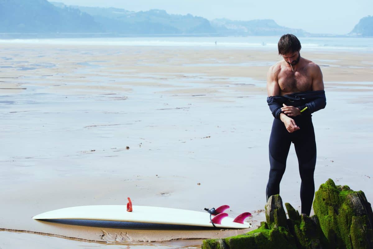 man removes his wetsuit standing on the beach