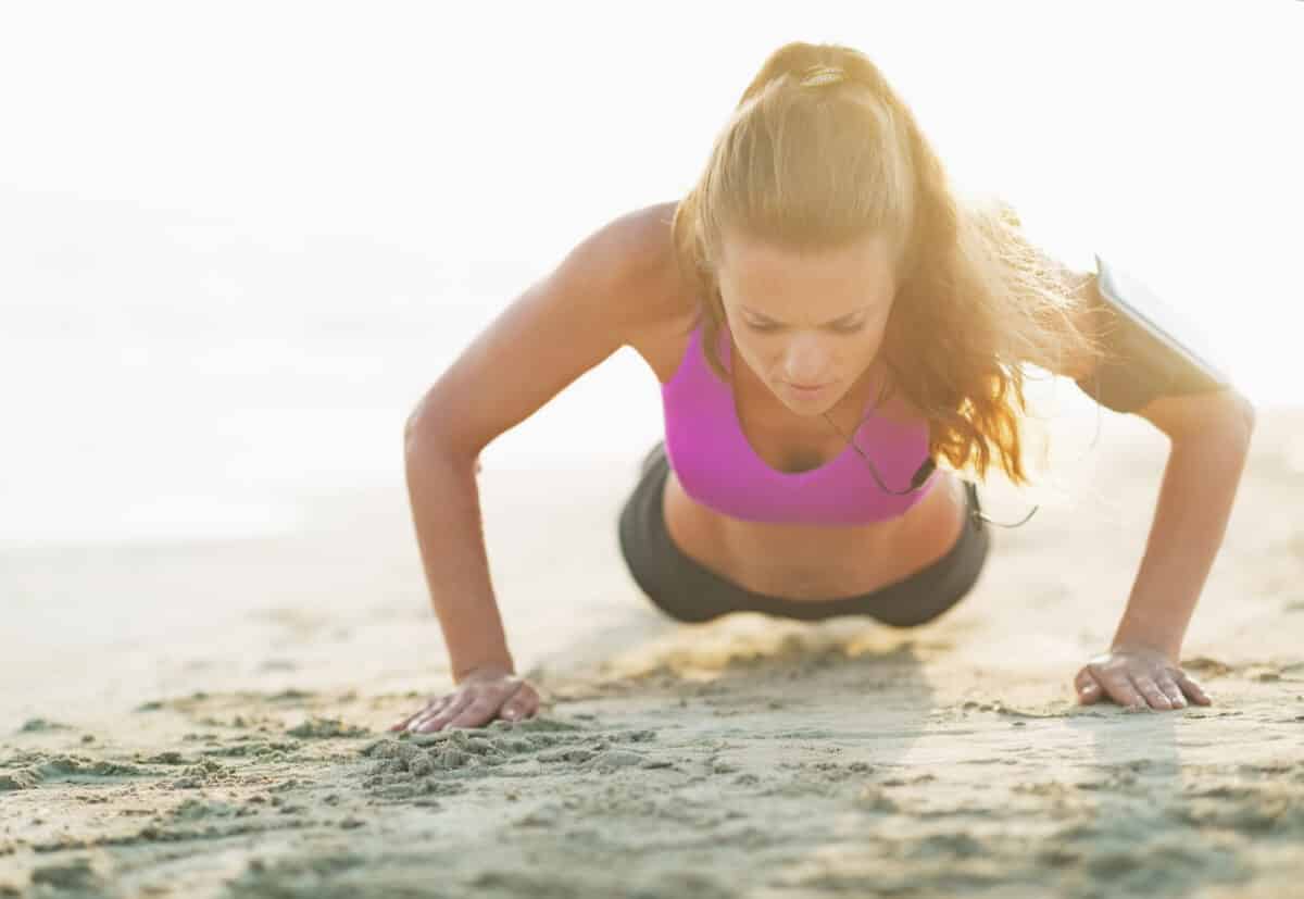 Young fitness woman on sand performing press ups