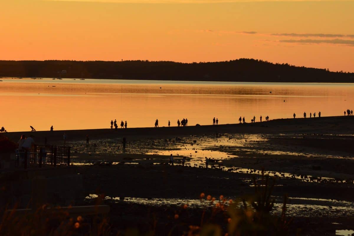 Sunset at a river with the tide out.  People walk along the shore line